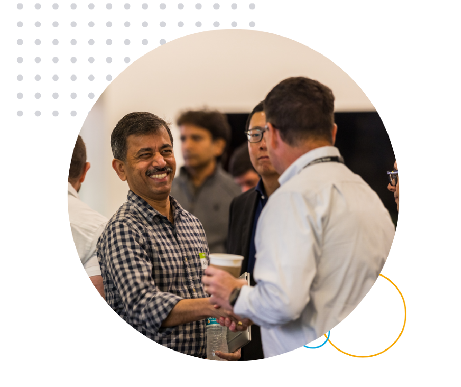 Website Graphic Header (8) Man in a checkered shirt smiles warmly while shaking hands with another person at a networking event. The atmosphere is friendly and engaging.